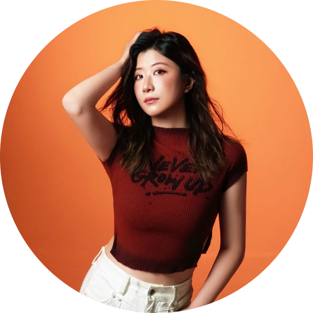 Norah Yang in a red Never Grow Up tee against a warm orange circle